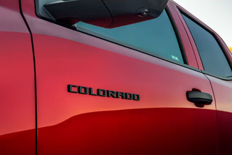 Send it Auto Parts black Colorado emblem installed on the side of a red Chevrolet truck door
